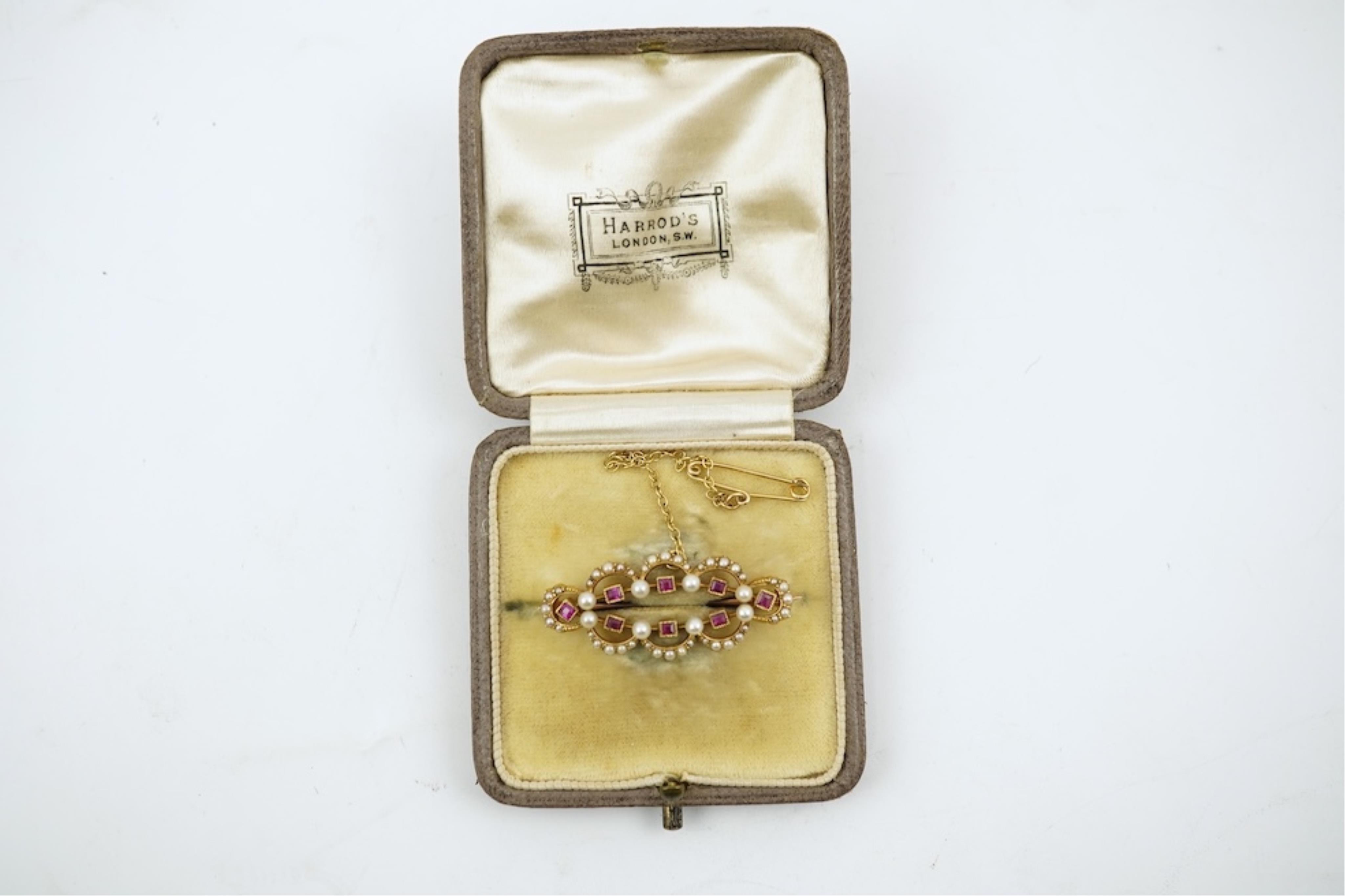 An Edwardian 15ct, ruby and seed pearl cluster set brooch, 33mm, with safety chain, gross weight 4.1 grams.